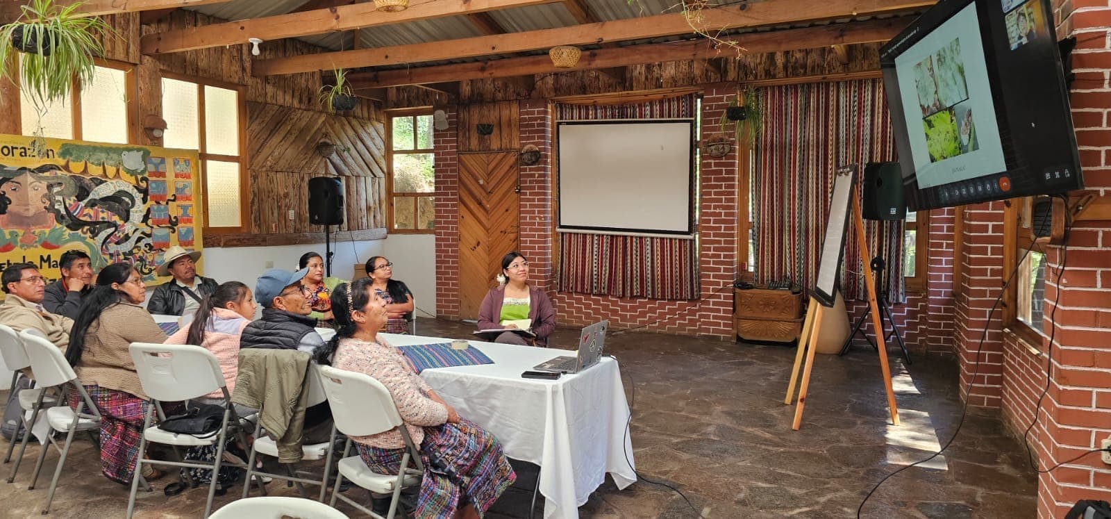 Taller comunitario en un salón de madera, con participantes reunidos frente a una proyección